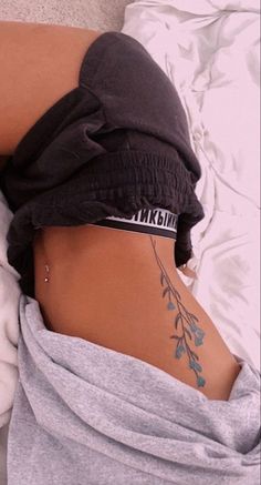 a woman laying in bed with her back turned to the side and tattoos on her stomach