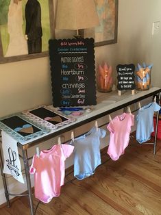 baby clothes are hung on the clothesline in front of a chalkboard with writing