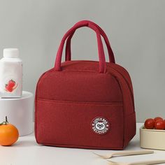 a red lunch bag sitting on top of a white table next to some oranges