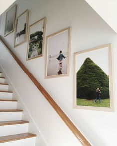 some pictures hanging on the wall next to a stair case in a house with white walls and wooden handrails