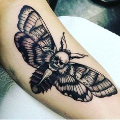 a black and white moth tattoo on the left arm, with a skull in the middle