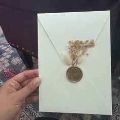 a person holding a white envelope with a wax stamp and dried flowers on the front