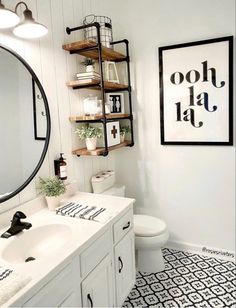 a white bathroom with black and white tile flooring on the walls, along with a round mirror above the sink