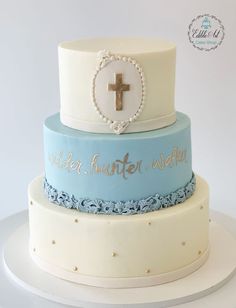 a three tiered cake with a cross on the top and words written below it