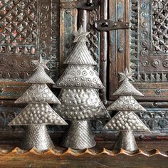 three metal christmas trees are on display in front of an ornately decorated wooden door