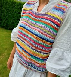 a woman wearing a multicolored crochet knitted vest in the grass