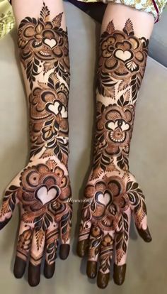 two hands with henna designs on them, one has hearts and the other has flowers