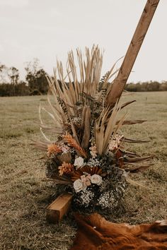 an arrangement of flowers and plants is placed on the ground in front of a wooden pole