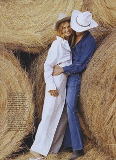 two people standing next to each other in front of hay bales with hats on