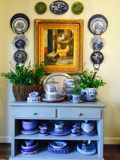 a blue and white china cabinet with plates on the wall next to it in front of a painting