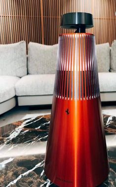 a red vase sitting on top of a marble floor next to a couch and coffee table