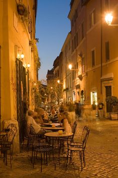 people sitting at tables in an alleyway with buildings on either side and street lamps