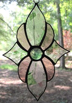 a stained glass sun catcher hanging from a tree in the woods with leaves on it