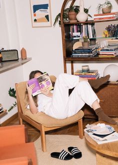 a woman sitting in a chair reading a book with her feet up on the floor