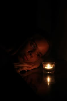 a woman sitting next to a candle in the dark