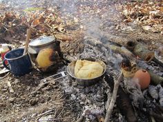 an open fire with pots and pans cooking food on the ground in front of it