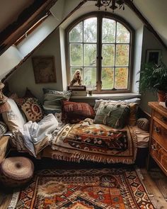 an attic bedroom with lots of pillows and rugs on the floor in front of a window