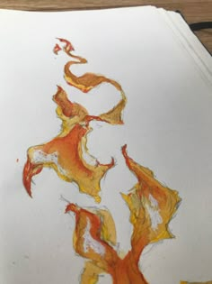 a piece of paper that has been drawn with orange and yellow paint on it, sitting on a table