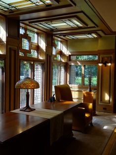 an office with lots of windows and a desk in front of the window has a lamp on it