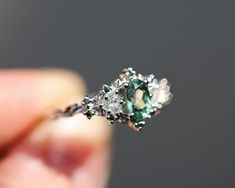 a close up of a person's hand holding a ring with an emerald and white diamond