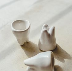 three white ceramic objects sitting on top of a table next to each other and one has a cup in the shape of a bird