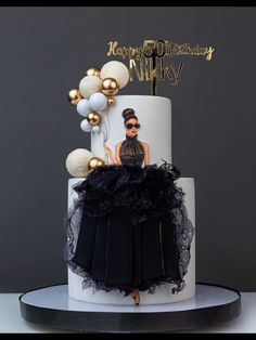 a white and black birthday cake with gold balloons on top is decorated with an image of a woman's face