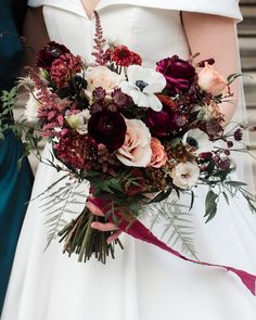 a close up of a bride holding a wedding bouquet with red and white flowers on it