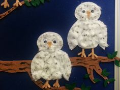 two white owls sitting on top of a tree branch with leaves and branches around them