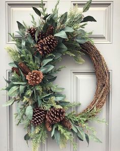 a wreath with pine cones and greenery is hanging on the front door to welcome guests