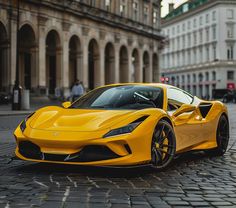 a yellow sports car parked in front of a large building on a cobblestone street