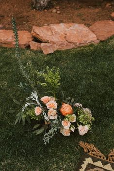 a bouquet of flowers sitting on top of a grass covered field next to rocks and a rug