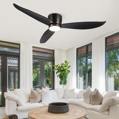 a living room with white couches and black ceiling fan in the middle of it