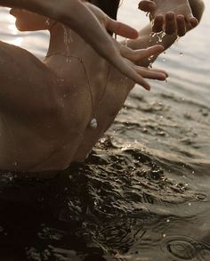 a woman in the water with her hands out to another person who is reaching for something