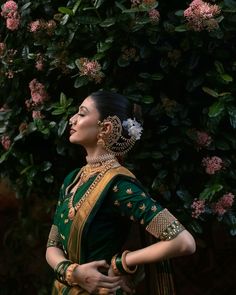 a woman in a green and gold sari standing next to a tree with pink flowers