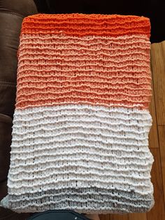 an orange and white crocheted blanket sitting on top of a couch