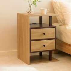 a nightstand with two drawers next to a bed and a plant on top of it