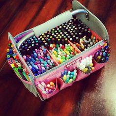 a pink case filled with lots of colored pencils on top of a wooden table