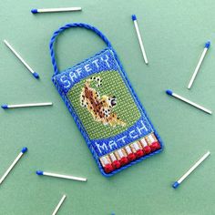 a cross - stitch bookmark with matches on it and some pins in the background