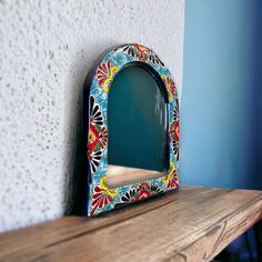 a wooden shelf with a colorful mirror on it's side next to a blue wall