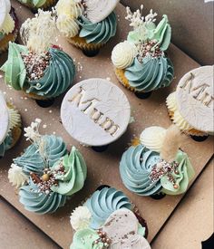 cupcakes decorated with frosting and flowers are on display in a cardboard box