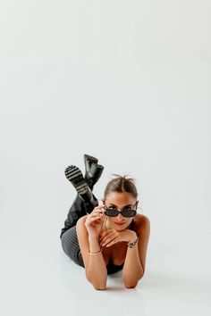 a woman laying on the ground with her hands behind her head wearing sunglasses and black pants