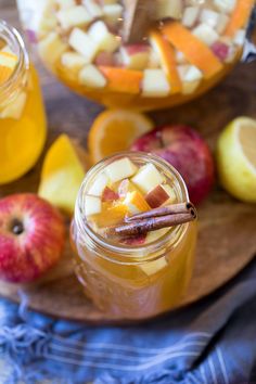 two jars filled with apple cider next to sliced apples and oranges on a plate