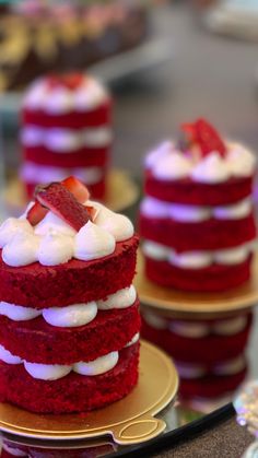 three red velvet cakes with white frosting and strawberries on top, sitting on gold plates