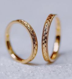 two gold wedding rings sitting on top of a white surface with one ring in the middle