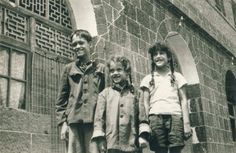 three children standing next to each other in front of a brick building with arched windows