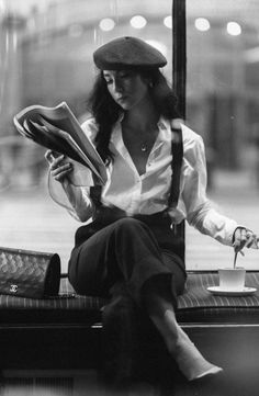 black and white photograph of a woman sitting on a window sill reading a book