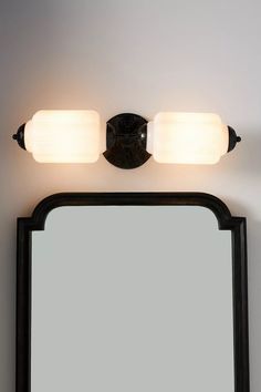 a bathroom vanity light with two lights on top of it and a mirror in front of it