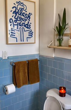 a bathroom with blue tiles and white fixtures, including a painting on the wall above the toilet