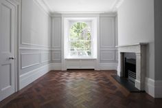 an empty room with wood flooring and a fireplace in the corner, painted white