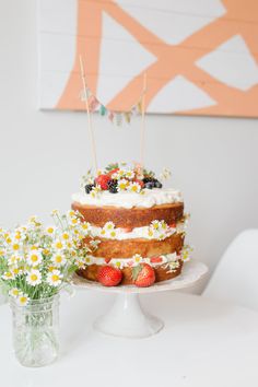 a cake sitting on top of a white plate next to flowers and a vase with strawberries